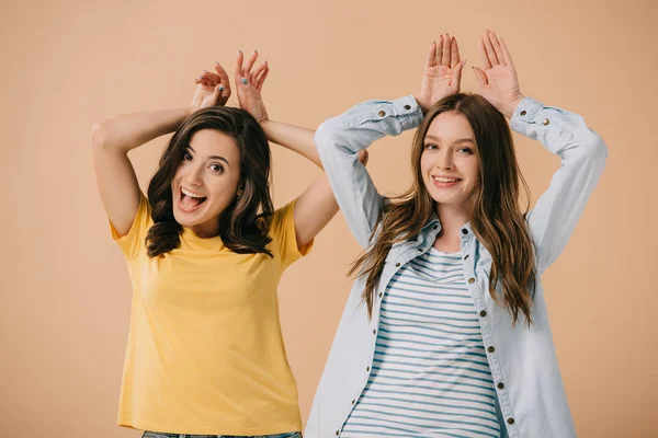 Attractive and smiling friends showing bunny ears with hands isolated on beige — Stock Photo