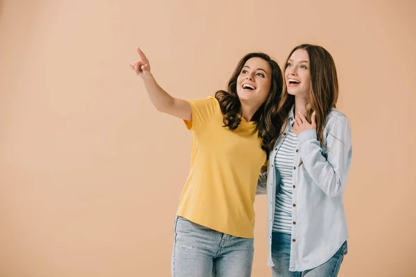 Attraktive und lächelnde Freunde, die mit dem Finger auf beige zeigen — Stockfoto