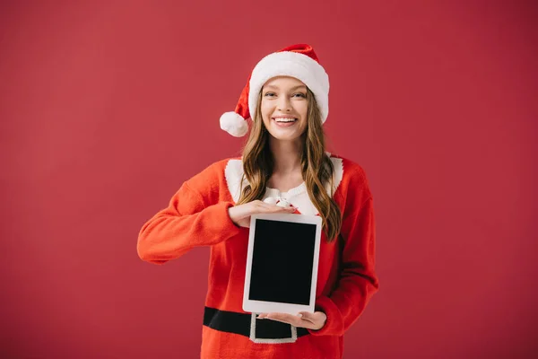 Attractive woman in santa hat and sweater holding digital tablet isolated on red — Stock Photo