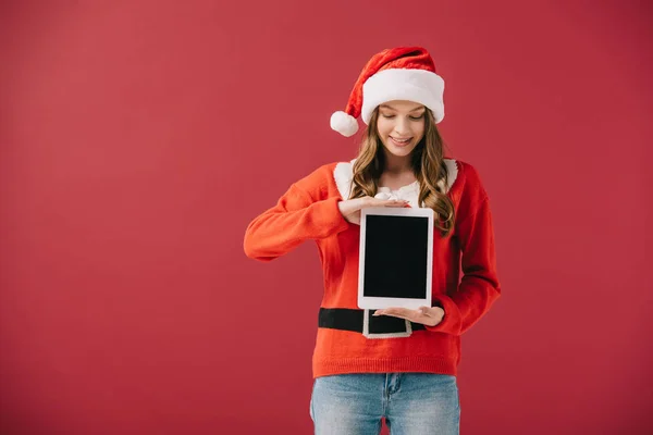 Attractive woman in santa hat and sweater holding digital tablet isolated on red — Stock Photo