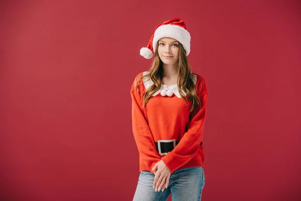 Attraente donna in cappello di Babbo Natale e maglione guardando la fotocamera isolata sul rosso — Foto stock
