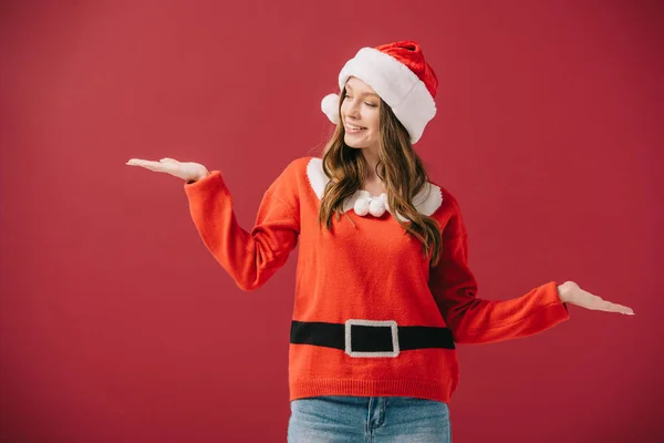 Attraktive Frau in Weihnachtsmütze und Pullover mit ausgestreckten Händen auf rotem Grund — Stockfoto