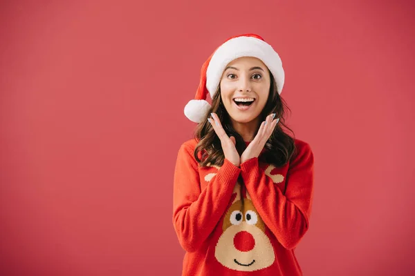 Attractive and smiling women in sweaters and santa hats looking at camera isolated on red — Stock Photo