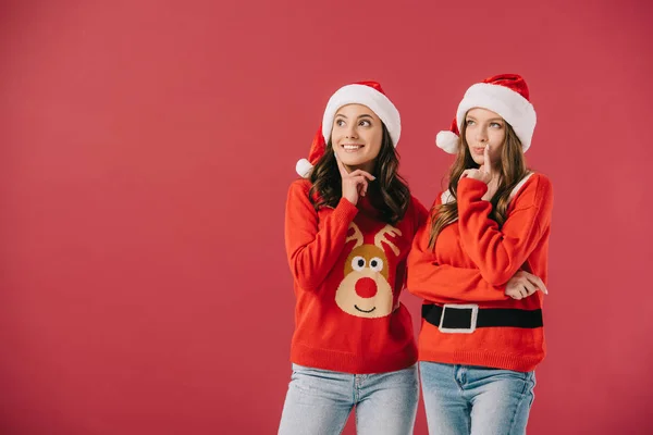 Attractive and pensive women in sweaters and santa hats looking away isolated on red — Stock Photo