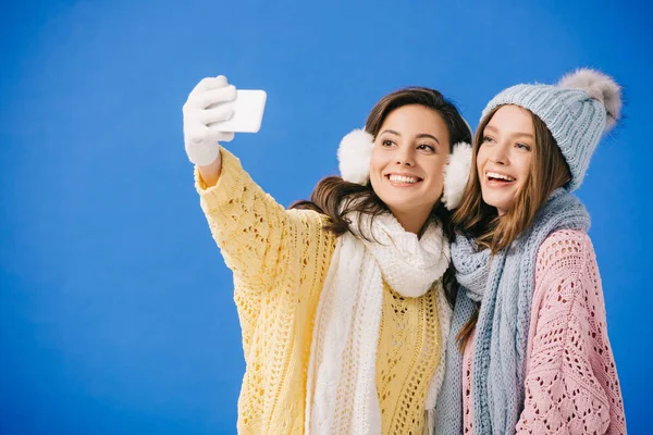 Jolies et souriantes femmes en chandails et foulards prenant selfie isolé sur bleu — Photo de stock