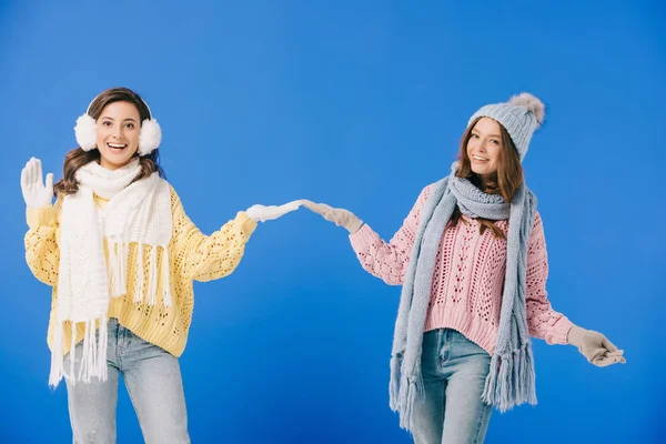 Femmes attrayantes et souriantes en chandails et écharpes avec les mains tendues isolées sur bleu — Photo de stock