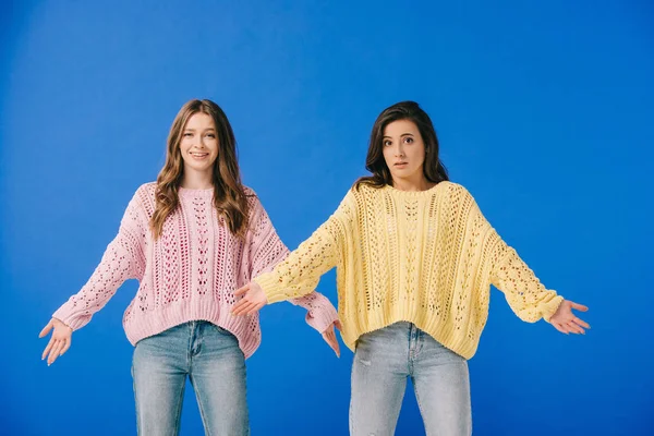 Attractive and shocked women in sweaters looking at camera isolated on blue — Stock Photo