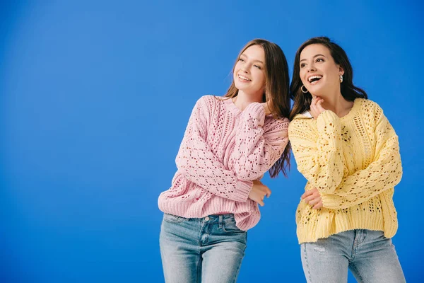 Attractive and smiling women in sweaters looking away isolated on blue — Stock Photo