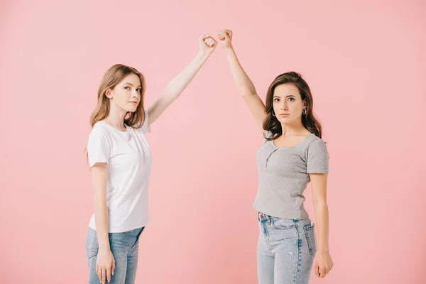 Привлекательные женщины в футболках, показывающие кулаки и смотрящие на камеру, изолированную на розовом — стоковое фото