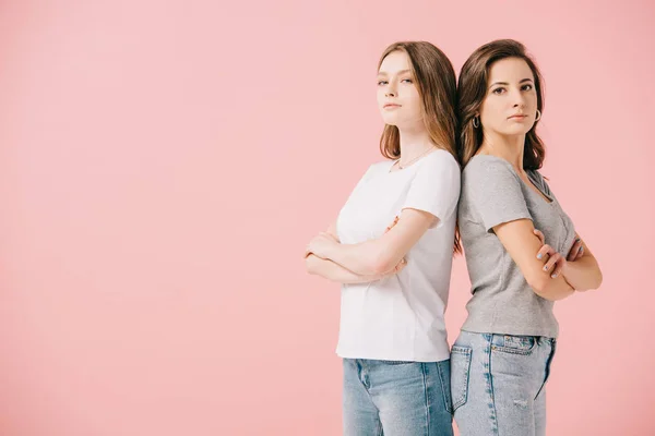 Mujeres atractivas en camisetas que muestran con brazos cruzados mirando a la cámara aislada en rosa - foto de stock