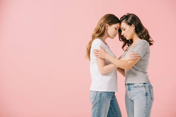 Side view of attractive women in t-shirts hugging isolated on pink — Stock Photo