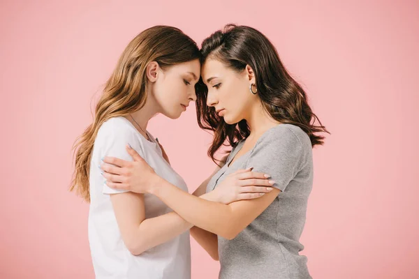 Seitenansicht attraktiver und trauriger Frauen in T-Shirts, die sich vereinzelt auf rosa umarmen — Stockfoto