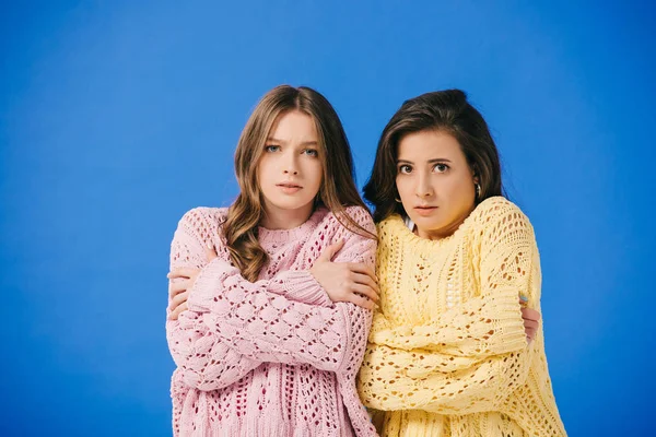 Attractive women in sweaters looking at camera and feeling cold isolated on blue — Stock Photo