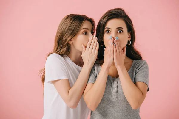 Attraente donna raccontando segreto per il suo amico scioccato in t-shirt isolato su rosa — Foto stock