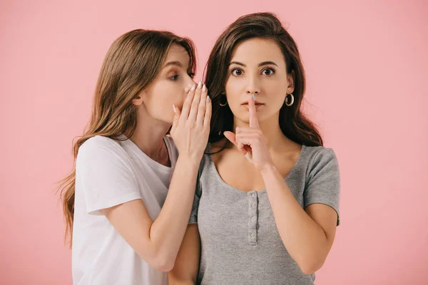 Attractive woman telling secret to her friend in t-shirt isolated on pink — Stock Photo