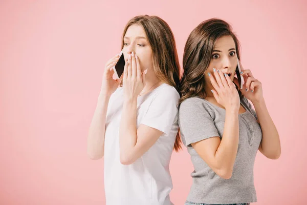 Mujeres atractivas y conmocionadas en camisetas hablando en teléfonos inteligentes aislados en rosa - foto de stock