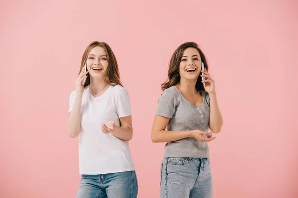 Mujeres atractivas y sonrientes en camisetas hablando en teléfonos inteligentes aislados en rosa - foto de stock