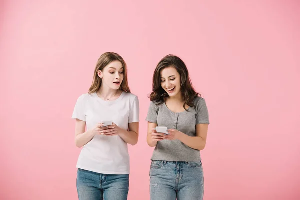 Attraktive und lächelnde Frauen in T-Shirts, die ihr Smartphone isoliert auf rosa halten — Stockfoto