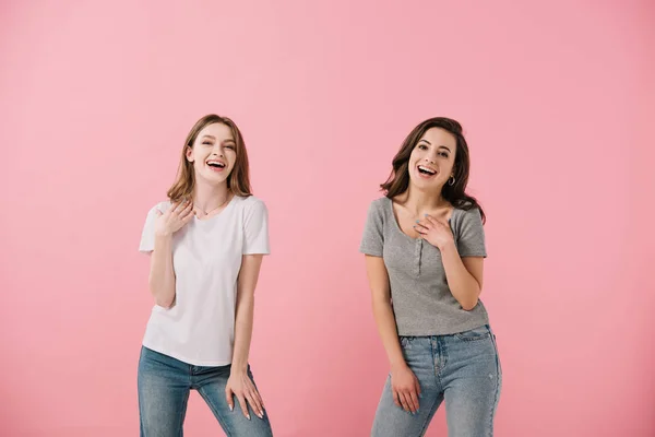 Привабливі і усміхнені жінки в футболках, дивлячись на камеру ізольовані на рожевому — стокове фото