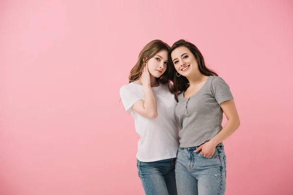 Привабливі і усміхнені жінки в футболках, дивлячись на камеру ізольовані на рожевому — стокове фото