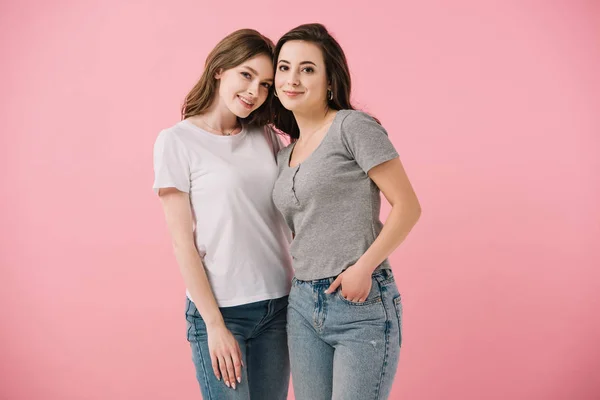Donne attraenti e sorridenti in t-shirt guardando la fotocamera isolata sul rosa — Foto stock