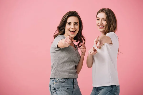 Mujeres atractivas y sonrientes en camisetas que señalan con los dedos aislados en rosa - foto de stock