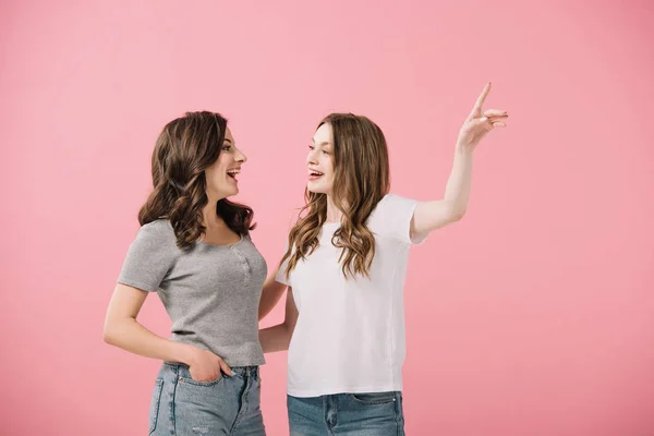 Donne attraenti e sorridenti in t-shirt che puntano con il dito isolato sul rosa — Foto stock