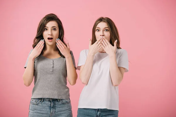 Mujeres atractivas y conmocionadas en camisetas mirando a la cámara aislada en rosa - foto de stock