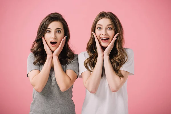 Attractive and shocked women in t-shirts looking at camera isolated on pink — Stock Photo