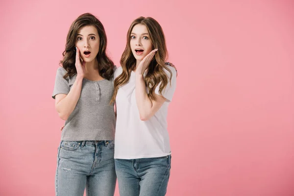 Привлекательные и шокированные женщины в футболках, смотрящие в камеру, изолированную на розовом — стоковое фото
