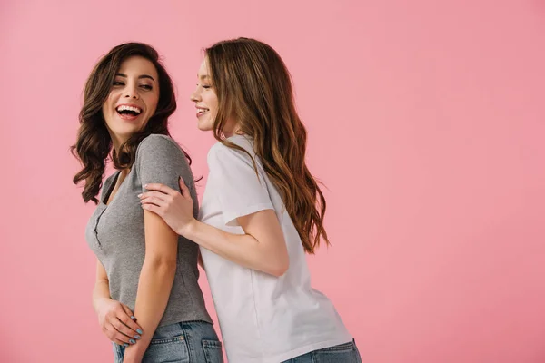 Mujeres atractivas y sonrientes en camisetas mirándose aisladas en rosa - foto de stock