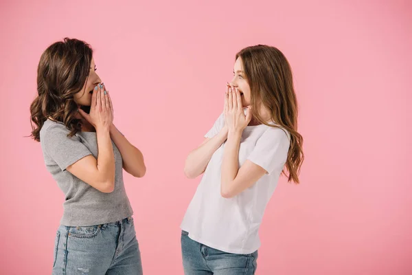 Attractive and shocked women in t-shirts looking at each other isolated on pink — Stock Photo