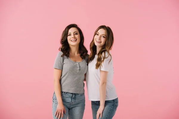 Mujeres atractivas y sonrientes en camisetas mirando a la cámara aislada en rosa - foto de stock