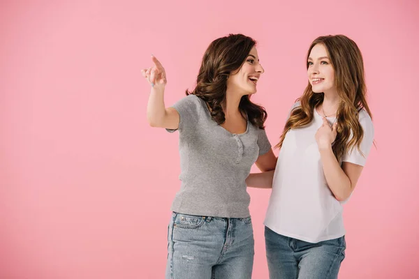 Donne attraenti e sorridenti in t-shirt che puntano con il dito isolato sul rosa — Foto stock
