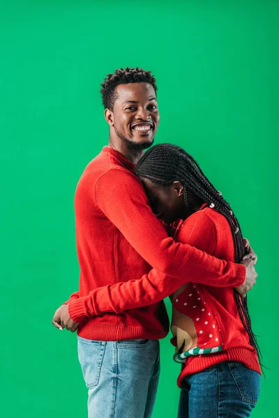 African American man hugging woman in red Christmas sweater isolated on green — Stock Photo