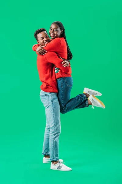 African American man holding up woman in red Christmas sweater isolated on green — Stock Photo
