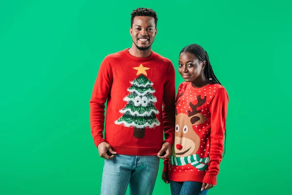 Uomo afroamericano vicino alla donna in maglioni di Natale rosso sorridente e guardando la fotocamera isolata sul verde — Foto stock