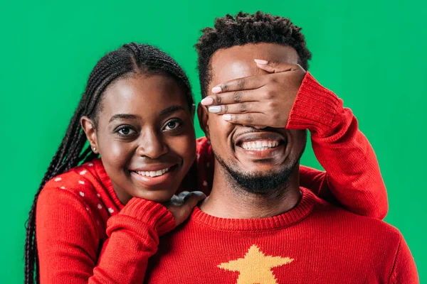 African American woman in red sweater covering eyes with hand to man isolated on green — Stock Photo