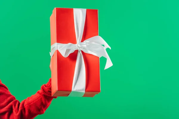 Cropped view of hand with red gift box with white ribbon isolated on green — Stock Photo