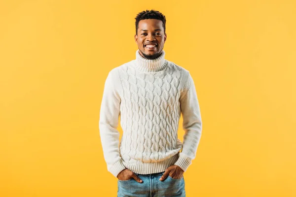 African American man in knitted sweater holding hands in pockets, smiling and looking at camera isolated on yellow — Stock Photo