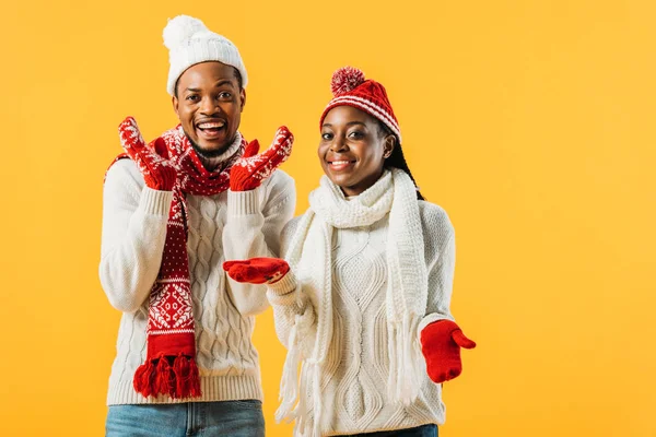 African American couple in knitted sweaters, scarfs and gloves smiling and looking at camera isolated on yellow — Stock Photo