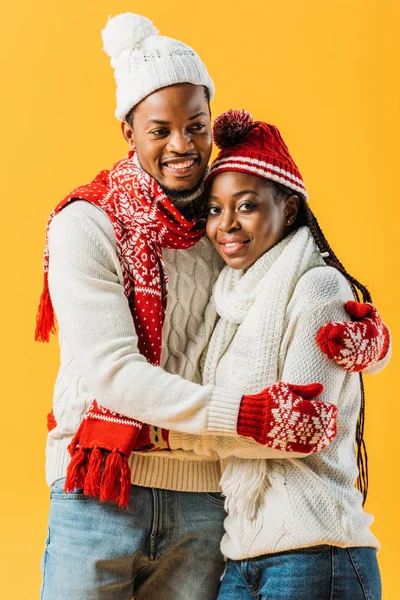 African American couple in cozy winter outfit looking at camera and hugging each other isolated on yellow — Stock Photo