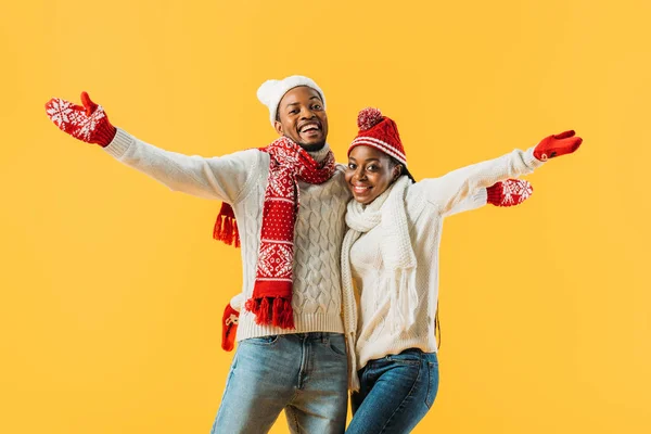 Afrikanisches amerikanisches Paar im gemütlichen Winteroutfit umarmt, die Hände ausgestreckt und vereinzelt in die Kamera auf gelb geschaut — Stockfoto