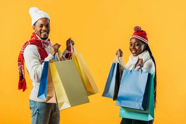 African American couple in winter outfit holding shopping bags isolated on yellow — Stock Photo