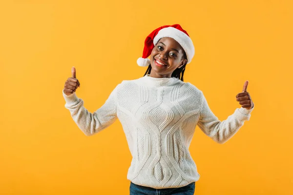 African American woman in winter sweater and Santa hat showing like signs isolated on yellow — Stock Photo