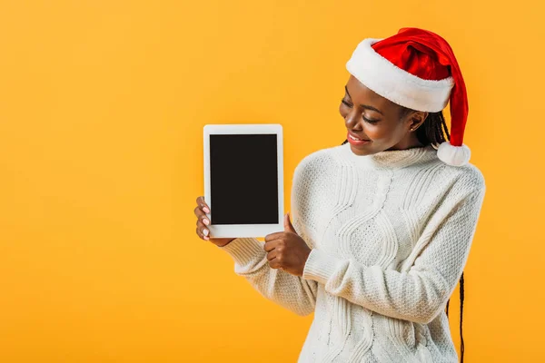 African American woman in winter sweater and Santa hat holding digital tablet with blank screen isolated on yellow — Stock Photo
