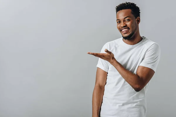 African American man in white T-short pointing with hand and looking at camera isolated on grey — Stock Photo