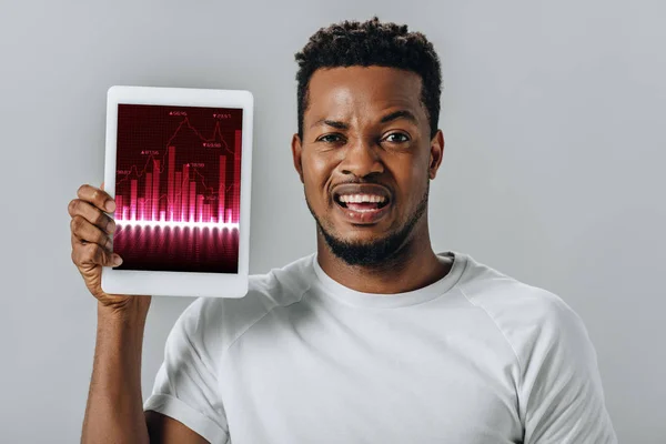 Bouleversé homme afro-américain tenant tablette numérique avec des cartes d'affaires et regardant la caméra isolée sur gris — Photo de stock