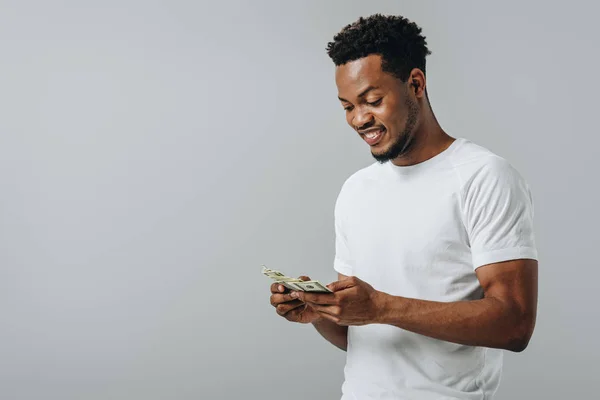 Hombre afroamericano contando billetes de dólar aislados en gris - foto de stock