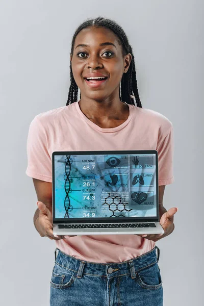 Excited African American woman holding laptop with medical data isolated on grey — Stock Photo